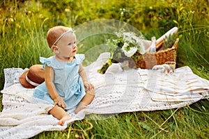 Adorable baby girl sitting on blanket at the park with basket and flowers, parents with beautiful toddler having a