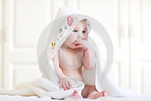 Adorable baby girl sitting under a hooded towel after bath