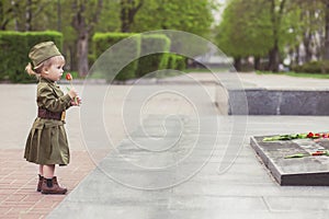 Adorable baby girl in Soviet military uniform lays a flower on a monument to those killed in World War II