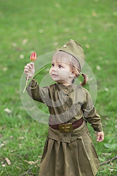 Adorable baby girl in Soviet military uniform with tulip in hands