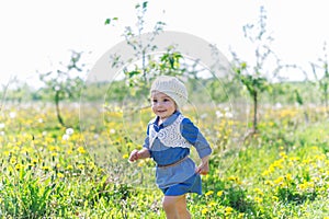 Adorable baby girl walking in green grass in forest lawn, playing and laughing