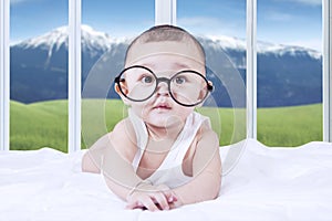 Adorable baby with glasses on bed