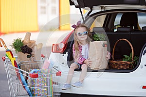 A little girl with a big trolley buys fresh food and vegetables in a big supermarket in the summer alone.