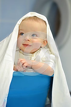 Adorable baby in a laundry basket in front of washing machine