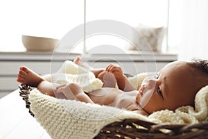 Adorable baby lying in wicker cradle by window