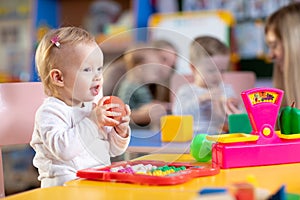 Adorable baby playing with educational toys with group of nursery kids under teacher supervision