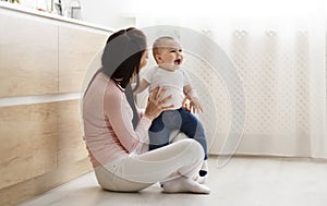 Adorable baby playing with mom, sitting on floor in kitchen