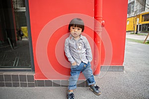 Adorable baby in a red shirt and jeans holding a hose standing in front of a red wall