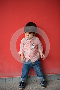 Adorable baby in red shirt and jeans standing in front of a red wall posing in various poses