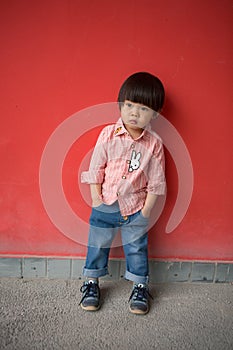 Adorable baby in red shirt and jeans standing in front of a red wall posing in various poses