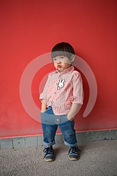 Adorable baby in red shirt and jeans standing in front of a red wall posing in various poses