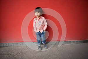 Adorable baby in red shirt and jeans standing in front of a red wall posing in various poses