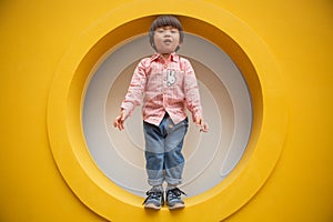 Adorable baby in red shirt and jeans standing in front of yellow hole wall