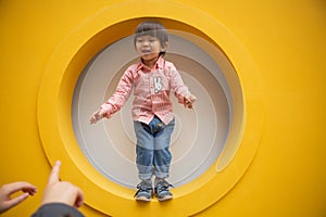 Adorable baby in red shirt and jeans standing in front of yellow hole wall