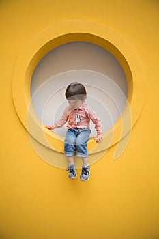 Adorable baby in red shirt and jeans standing in front of yellow hole wall