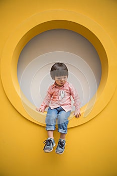 Adorable baby in red shirt and jeans standing in front of yellow hole wall