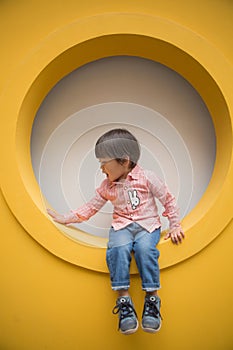 Adorable baby in red shirt and jeans standing in front of yellow hole wall