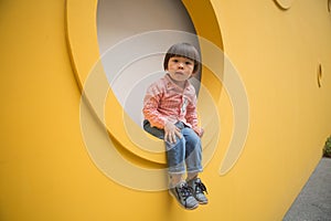 Adorable baby in red shirt and jeans standing in front of yellow hole wall