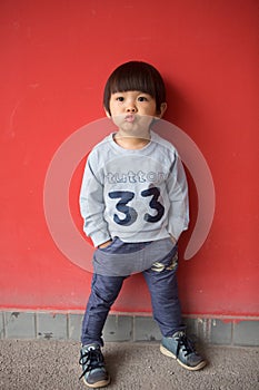 Adorable baby in stylish clothes posing in front of red wall