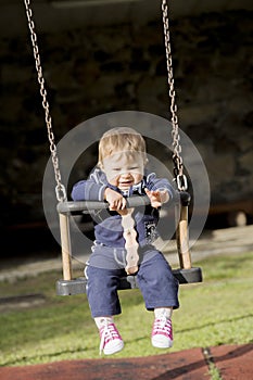 Adorable baby on swing pulling her arm while looking down