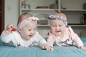 Adorable baby twins having fun in bed at home. Cute kids with hairbands ribbons, smiling, laughing. Happiness concept