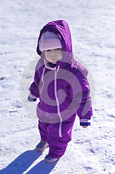 Adorable baby in a white snow in the warm suit siting in the snow
