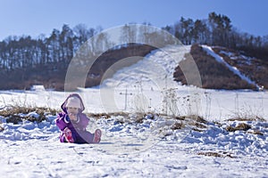 Adorable baby in a white snow in the warm suit siting in the snow