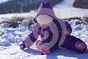 Adorable baby in a white snow in the warm suit siting in the snow