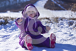 Adorable baby in a white snow in the warm suit siting in the snow