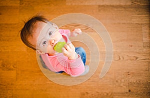 Adorable baby on wooden floor looking up with rubber toy in mouth. Copy space on right