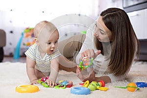 Adorable baby and young woman playing in nursery. Happy family having fun with colorful toy at home.