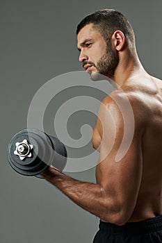 Adorable bearded male developing definition of muscles isolated on grey background