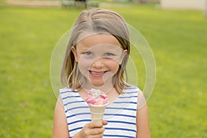 Adorable and beautiful blond young girl 6 or 7 years old eating delicious ice cream smiling happy on green grass field ba