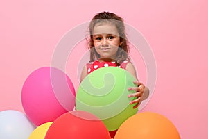 Adorable beautiful child, baby girl, 4 years kid hugging colorful balloons, isolated over pink background with copy space.