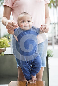 Adorable bi-racial baby boy learning to walk with the help of his mother