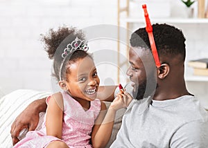 Adorable black baby girl putting lipstick on her dad lips
