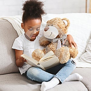 Adorable black kid with teddy bear reading book
