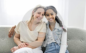 Adorable black teen daughter with mother sit on sofa at home