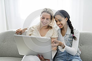 Adorable black teen daughter with mother sit on sofa at home with laptop