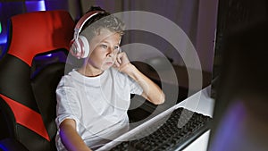 Adorable blond boy streamer, engrossed playing a futuristic video game, streaming live from his digital gaming room at night using
