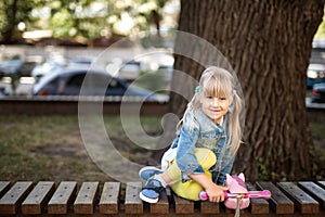 Adorable blond caucasian preschooler fashionista girl wearing jeans and bright yellow leggins sitting over wooden bench and