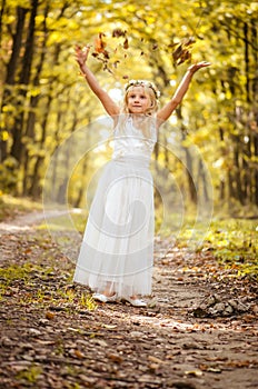 Adorable blond girl with leaves in hands in sunny day in magical forest