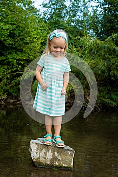 Adorable blond preschool girl playing in river