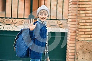 Adorable blond student kid saying goodbye with hand getting in the school