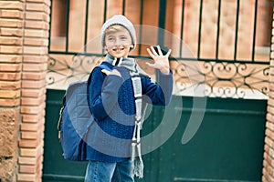 Adorable blond student kid saying goodbye with hand getting in the school