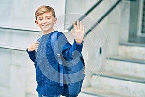 Adorable blond student kid saying goodbye with hand getting in the school