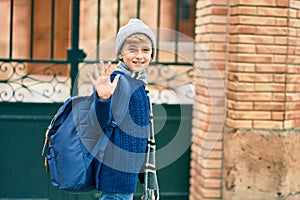 Adorable blond student kid saying goodbye with hand getting in the school