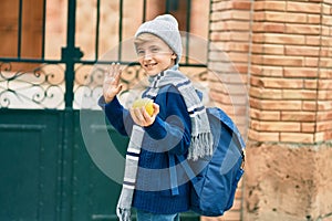 Adorable blond student kid saying goodbye with hand getting in the school