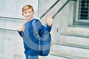 Adorable blond student kid saying goodbye with hand getting in the school