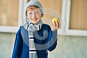 Adorable blond student kid smiling happy holding green apple at the school